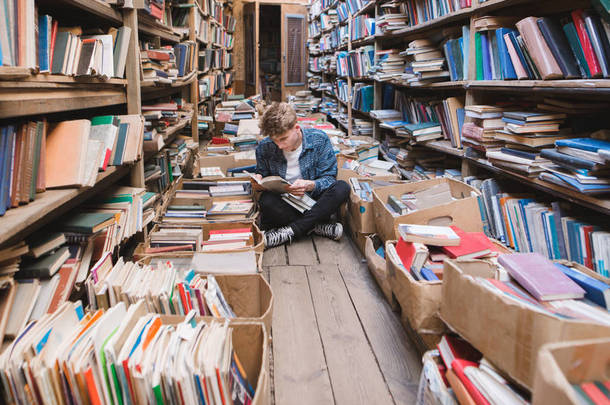 年轻的男子坐在地板上的旧公共图书馆和阅读书籍。学习这个概念。学生将在图书馆接受自我教育.