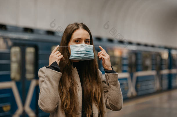 一名妇女戴上医疗面罩，以避免在<strong>地铁站</strong>传播高头牛病毒。一个穿着长发外套的女孩正在<strong>地铁站</strong>的月台上等火车.