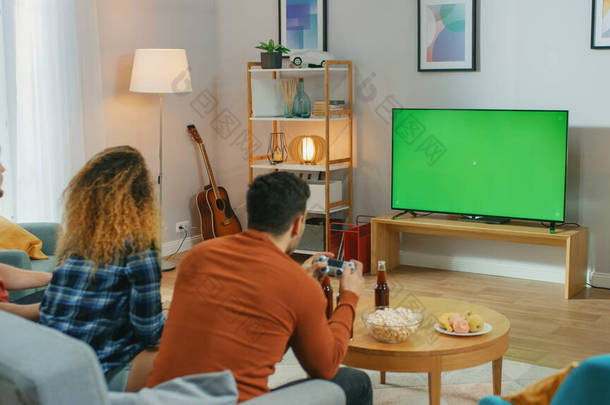 在客厅里，三位朋友在绿色的彩色键盘屏幕上玩电子游戏，他们使用的是控制装置。 <strong>在家</strong>里玩乐的青少年.