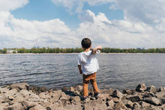 在蓝色河边抱着岩石的可爱男孩的倒影 