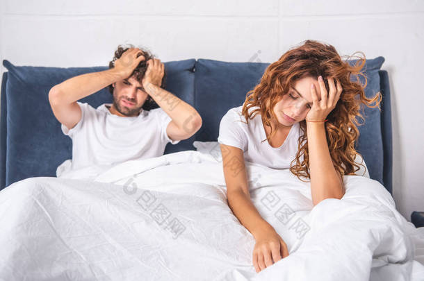年轻夫妇坐在床上, 在早上头痛的痛苦
