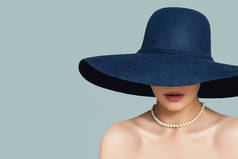 完美的女人在时尚的帽子和白色珍珠珠宝项链在蓝色背景 