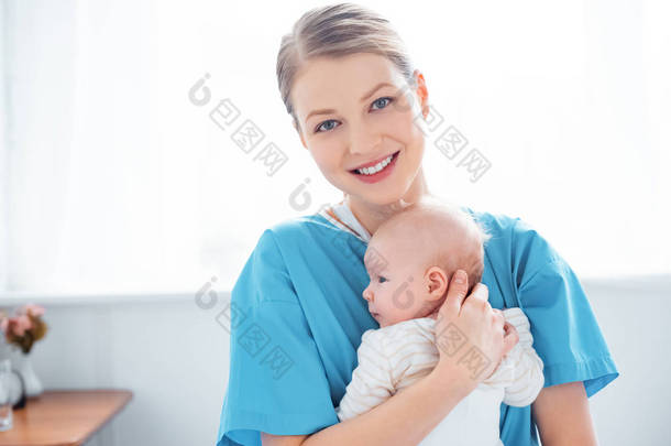 快乐的年轻母亲抱着新生的婴儿, 微笑着在医院房间里的镜头