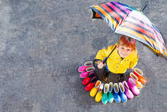 小小孩男孩和组的彩色雨靴。金发碧眼的孩子站在伞下。做和不同橡胶靴子，从高角度的特写镜头。多雨的秋天鞋靴