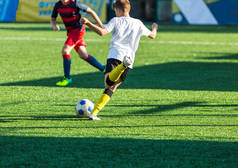 橄榄球队--红、蓝、白运动服的男孩们在绿色的田野上踢足球。男孩运球。运球技巧。团队游戏, 培训, 积极的生活方式, 爱好, 运动的孩子概念