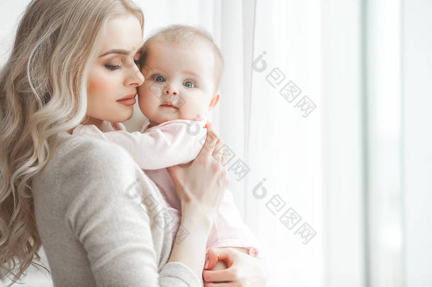年轻的<strong>母亲</strong>照顾她的小女儿。美丽的妈妈和她的女儿在室内的卧室里。爱的家人。迷人的妈妈抱着她的孩子.