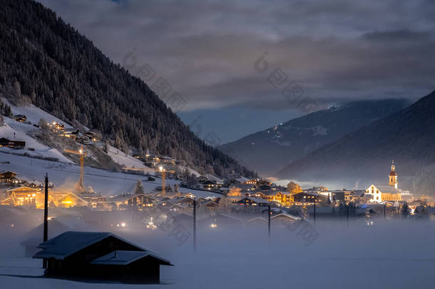 冬季的夜景俯瞰着奥地利的提洛里亚<strong>城市</strong>Neustift和普法尔教堂，背景是群山和云彩。 寒冷的夜晚，雾气弥漫山谷