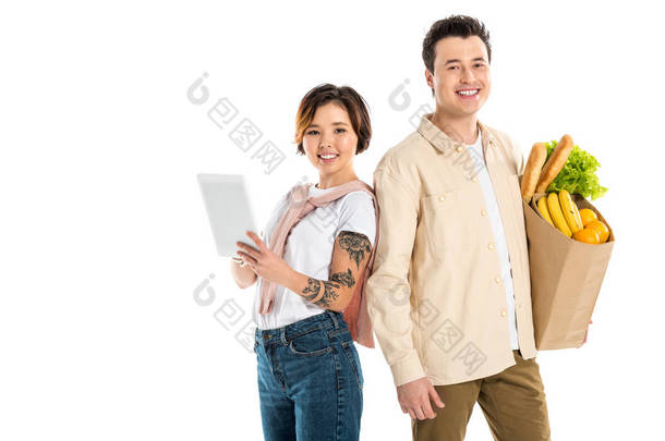 幸福的丈夫拿着购物袋, 而妻子使用数字平板电脑孤立在白色