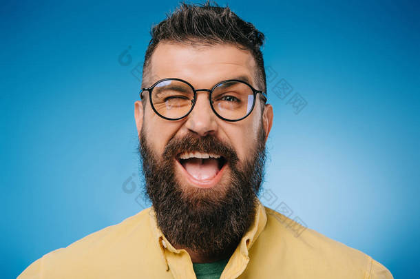 兴奋的胡须男子在眼镜眨眼隔离在蓝色