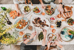家人或朋友聚餐。平装人的手与烤羊肩, 沙拉, 蔬菜, 葡萄酒, 含羞草树枝在白色格子桌布, 顶视图。庆祝派对晚宴