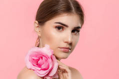 特写肖像一个美丽的年轻女孩与粉红色的玫瑰花隔离在粉红色背景.