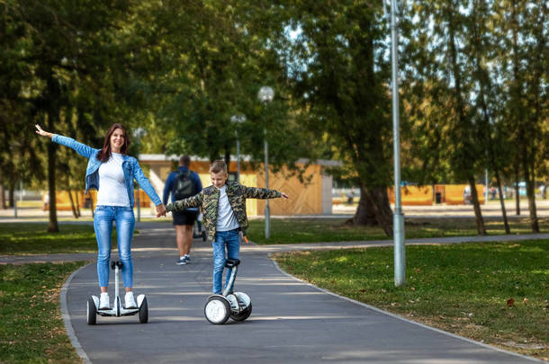 妈妈和儿子在公园里骑着一个<strong>气垫</strong>板，一个自平衡的滑板车。积极的生活方式时间与婴儿技术的未来