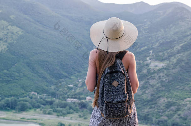 带着背包头戴帽子的年轻女子的背景图，背景在山谷中.