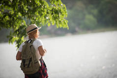 年轻快乐的女人背着背包站在那里看着河边。妇女旅行概念.