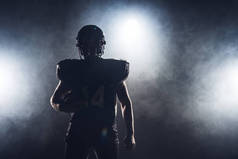装备美国橄榄球运动员的黑暗的剪影与球反对白色烟雾