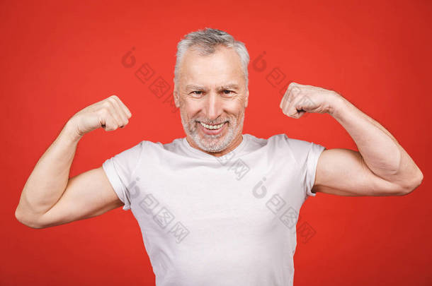 看看这个！老男人表现出肌肉。在红色的背景下,<strong>老年人</strong>把胳膊弯曲,与外界隔绝.兴高采烈的现代酷退休老人爷爷锻炼身体.