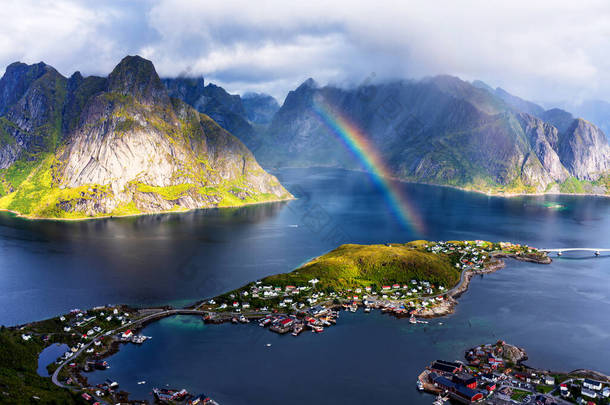 从Reinebringen山脊俯瞰挪威Lofoten岛上令人震惊的高山和Reine村的阳光鸟瞰全景。有彩虹和崎岖山峰的风景美景.