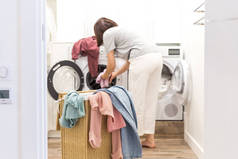 年轻女子在洗衣房装洗衣机和装满脏衣服的篮子