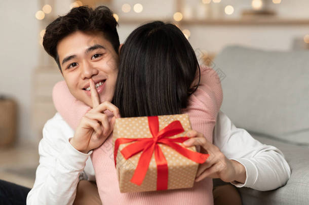 亚洲丈夫带着礼物举手投足拥抱女友坐在室内