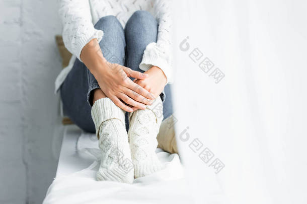 坐在公寓里穿着白色毛衣和牛仔裤的女人的裁剪视图 