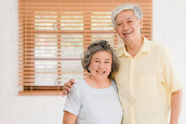 亚洲老年夫妇感到幸福的<strong>微笑</strong>，看着相机，而放松在客厅在家里。享受时间生活方式老年家庭在家里的概念。照看相机的肖像.