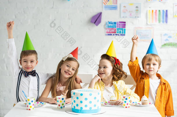 快乐的孩子们坐在聚会帽与<strong>蛋糕</strong>和庆祝生日在一起