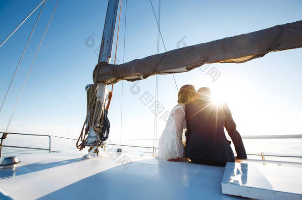 美丽<strong>的</strong>新婚夫妇在海上<strong>的</strong>婚宴上坐在游艇上。 漂漂亮亮<strong>的新娘</strong>身穿白色<strong>婚纱</strong>，穿着时髦<strong>的</strong>新郎乘坐豪华游艇在海上航行。 在一起。 婚礼日.