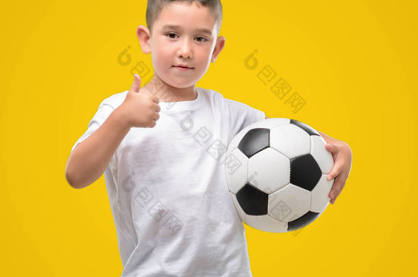 黑头发的小孩子玩足球高兴与大微笑做 ok 标志, 拇指与手指, 优秀的标志
