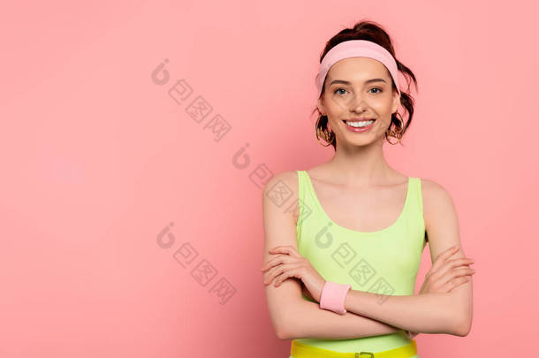 快乐的年轻女子，头戴头巾，<strong>交叉</strong>着双臂，面带微笑地站在粉色上 