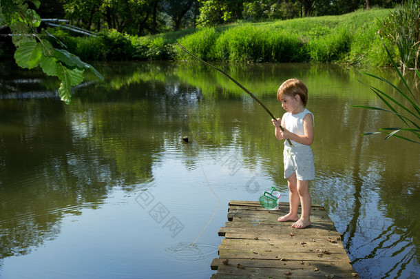 可爱的小男孩从边缘的木码头钓鱼和耐心地等着他的猎物，在阳光明媚的日子