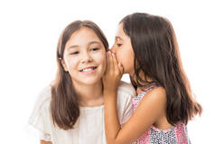 可爱的小妹妹分享有趣的秘密与姐姐在耳朵反对白色背景在演播室 