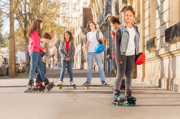 快乐十几岁的女孩穿着轮滑鞋站在镇上与她的朋友