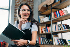 年轻微笑高加索女人抱着笔记本，远看图书馆