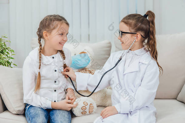 好奇的女孩在玩游戏：<strong>医生</strong>和病人。 <strong>小医生</strong>通过听诊器听病人的心跳.