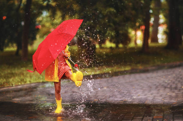 快乐的孩子女孩用伞和橡胶靴在秋天的沃尔玛的水坑里