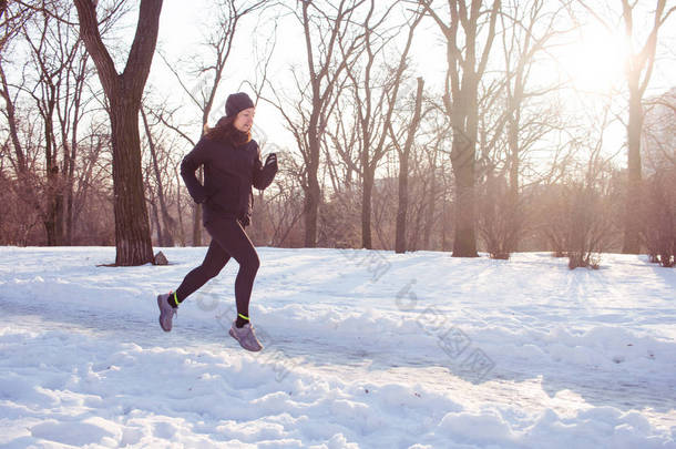 年轻女子运动员在黑色运动服奔跑在冬天公园