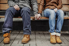 穿着牛仔裤和粗靴子、可爱的嬉皮士夫妇坐在长椅上手牵手