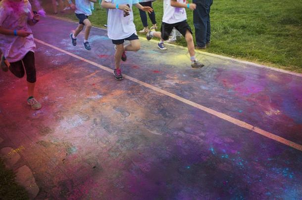 一组赛跑选手在一个颜色赛跑比赛中的抽象照片。在赛跑者的腿和脚和鞋子上没有可见的面孔。许多五颜六色的粉笔云在空中和街道上