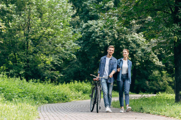 快乐的年轻夫妇走在公园与老式自行车