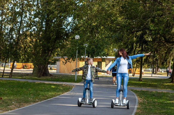 妈妈和儿子在公园里骑着一个气垫板，一个自平衡的滑板车。积极的生活方式时间与婴儿技术的未来