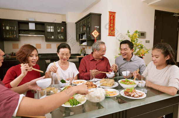 一群欢快<strong>的</strong>亚洲人在餐桌上享用美食，为泰特服务，在背景中献上<strong>对联</strong>，祝愿来年<strong>的</strong>到来