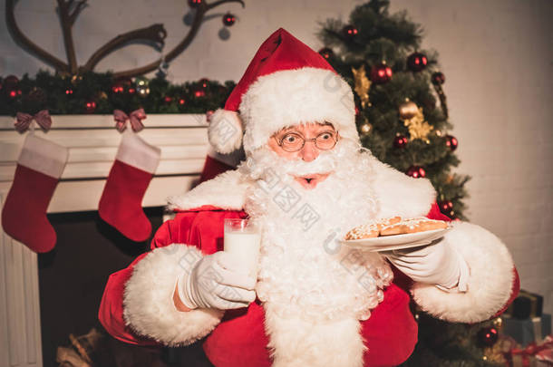 情绪化的圣诞老人举行与饼干和牛奶玻璃板