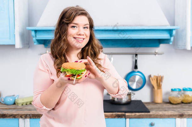 年轻超重妇女的肖像在厨房的手汉堡在家里