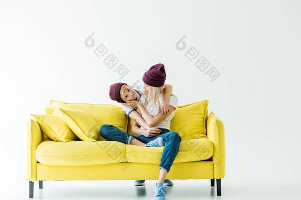 母亲和儿子在勃艮第帽子拥抱白色的黄色沙发上