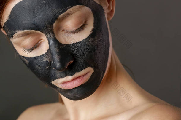 焦炭面罩或黑色粘土泥.漂亮的女人，脸上戴着黑色面具，近距离拍摄工作室的头像。天然化妆品概念.