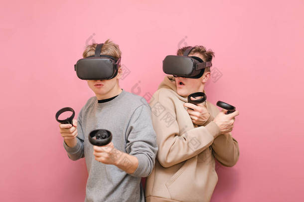 两个穿着Vr头盔的有趣玩家在粉色背景下，一起玩虚拟现实游戏，并在情感上做出反应。两名在粉色背景上被隔离的<strong>年轻人</strong>在控制器上玩Vr游戏