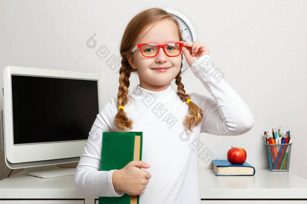 可爱的小女孩戴着<strong>眼镜</strong>，手里拿着一本书。 这个孩子是在学生工作场所的背景下长大的