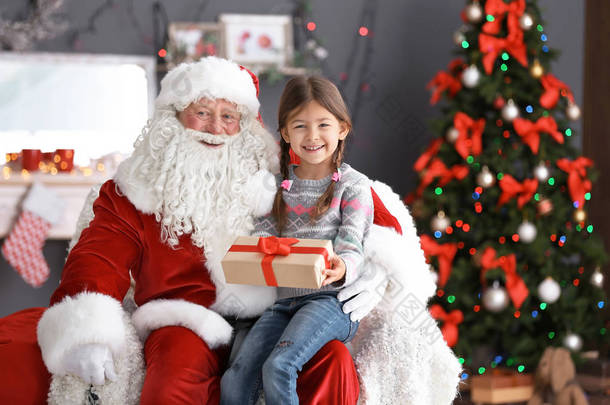 带礼品盒的小女孩坐在正宗的圣诞老人的大腿上