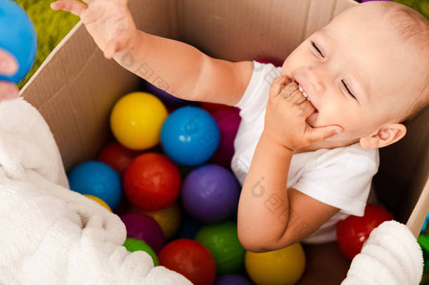可爱的孩子坐在纸板箱与五颜六色的球，笑和举手