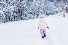 穿暖衣服的小孩子在冬天公园里漫步在雪地上